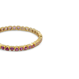 A gold eternity-style band bracelet featuring small heart-shaped pink gemstones set along the front, photographed on a clean white background.