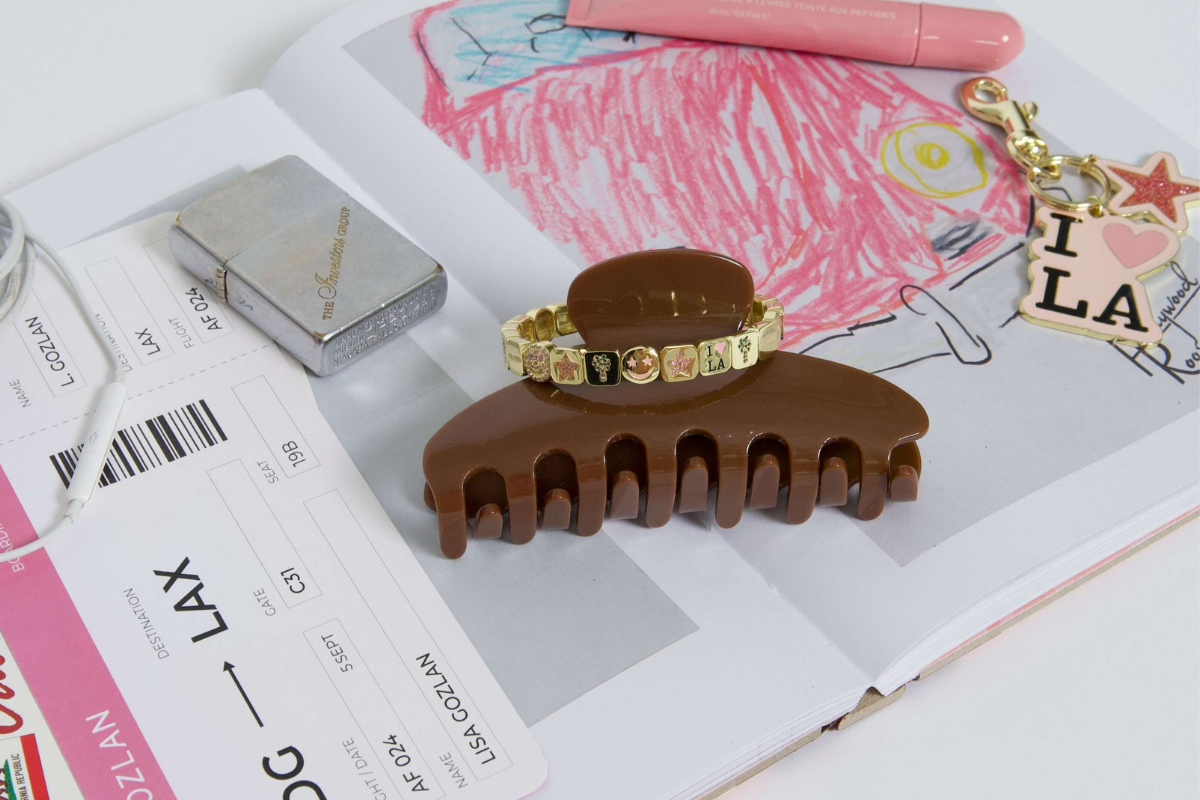 Brown hair clip with gold bracelet on top of an open book with drawings and text.