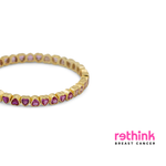 A gold eternity-style band bracelet featuring small heart-shaped pink gemstones set along the front, photographed on a clean white background.