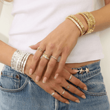 Close-up of hands wearing multiple gold and silver bracelets and rings on a white background