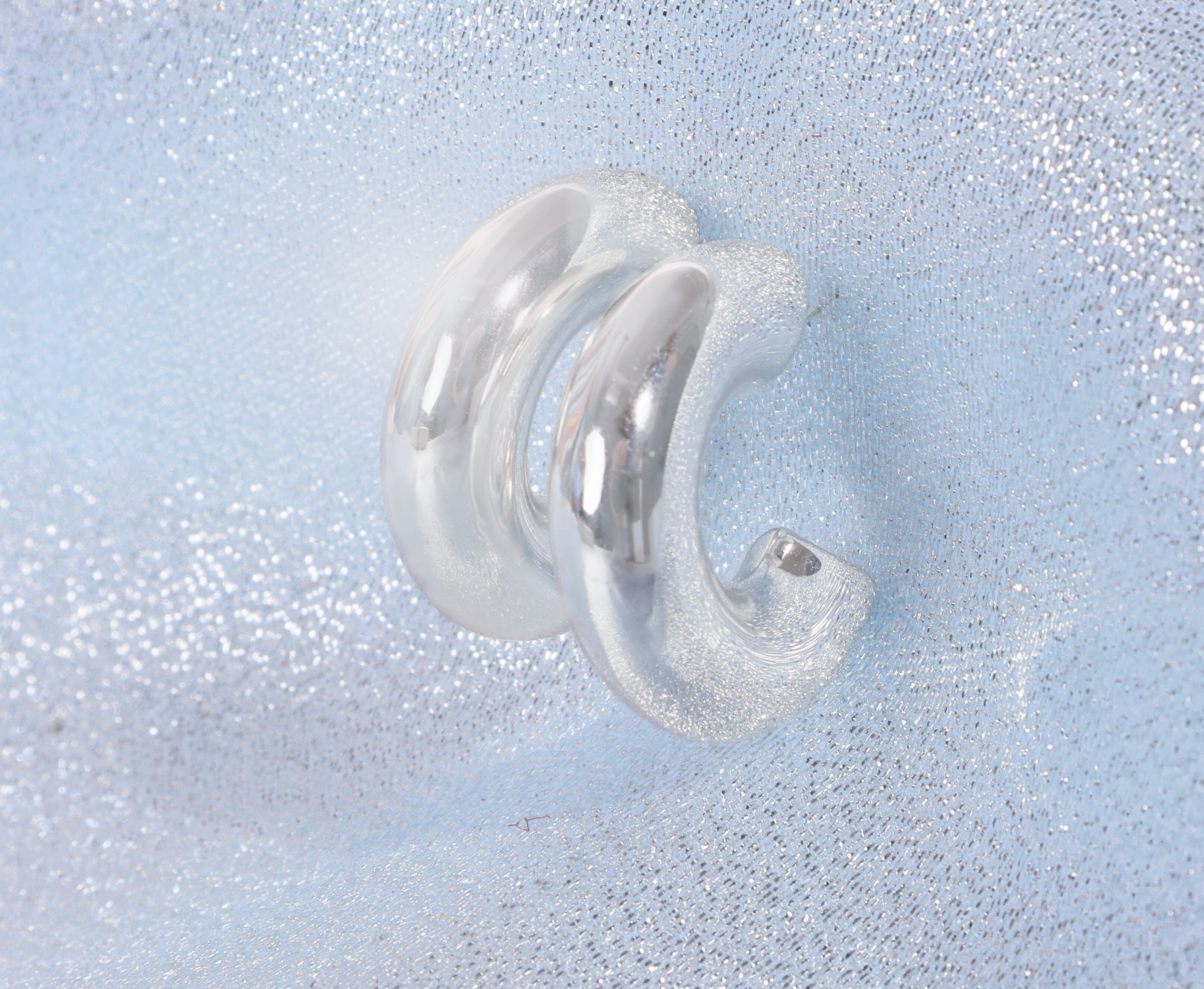 Silver earring on a textured light blue background