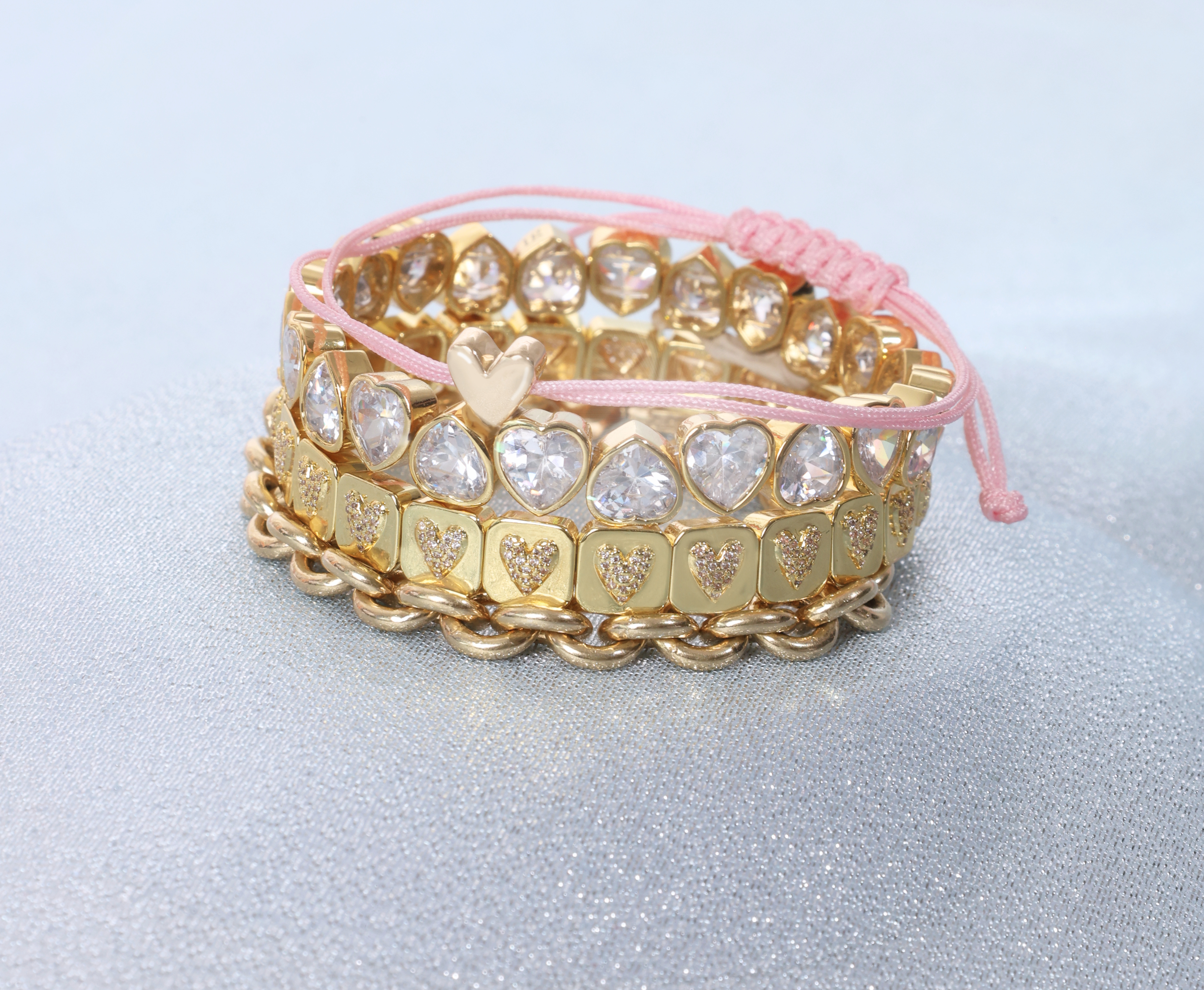 Stack of gold and silver heart-patterned bracelets on a light blue background