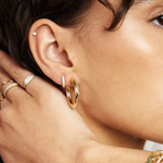 Close-up of a woman wearing gold hoop earrings with a hand adjusting them.