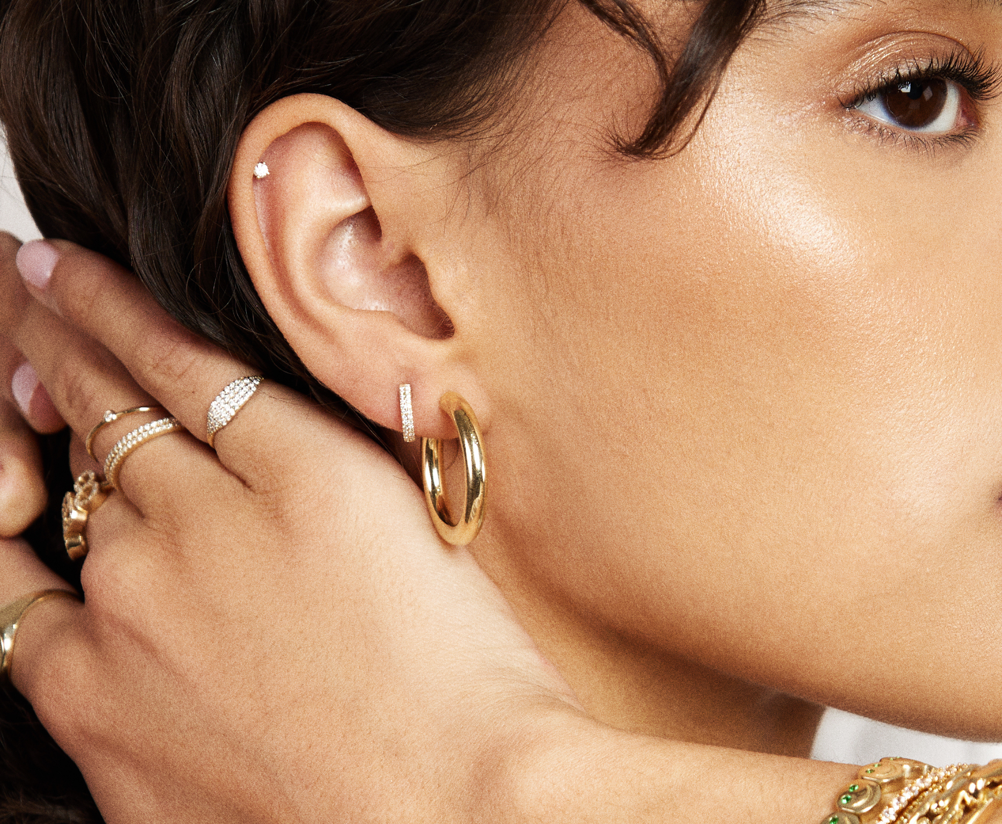 Close-up of a woman wearing gold hoop earrings with a hand adjusting them.