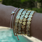 Wrist with multiple bracelets featuring various charms against a blurred natural background