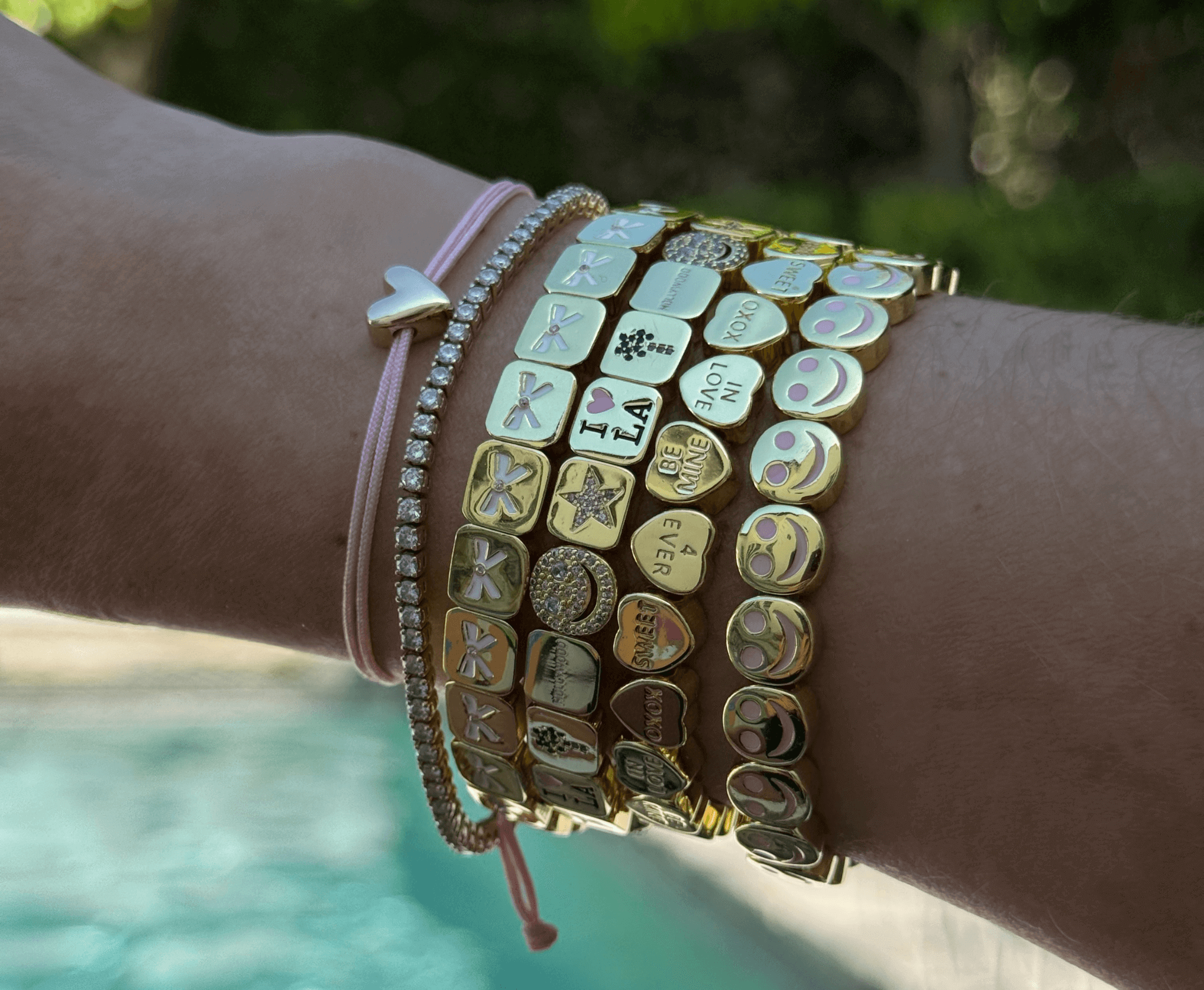 Wrist with multiple bracelets featuring various charms against a blurred natural background