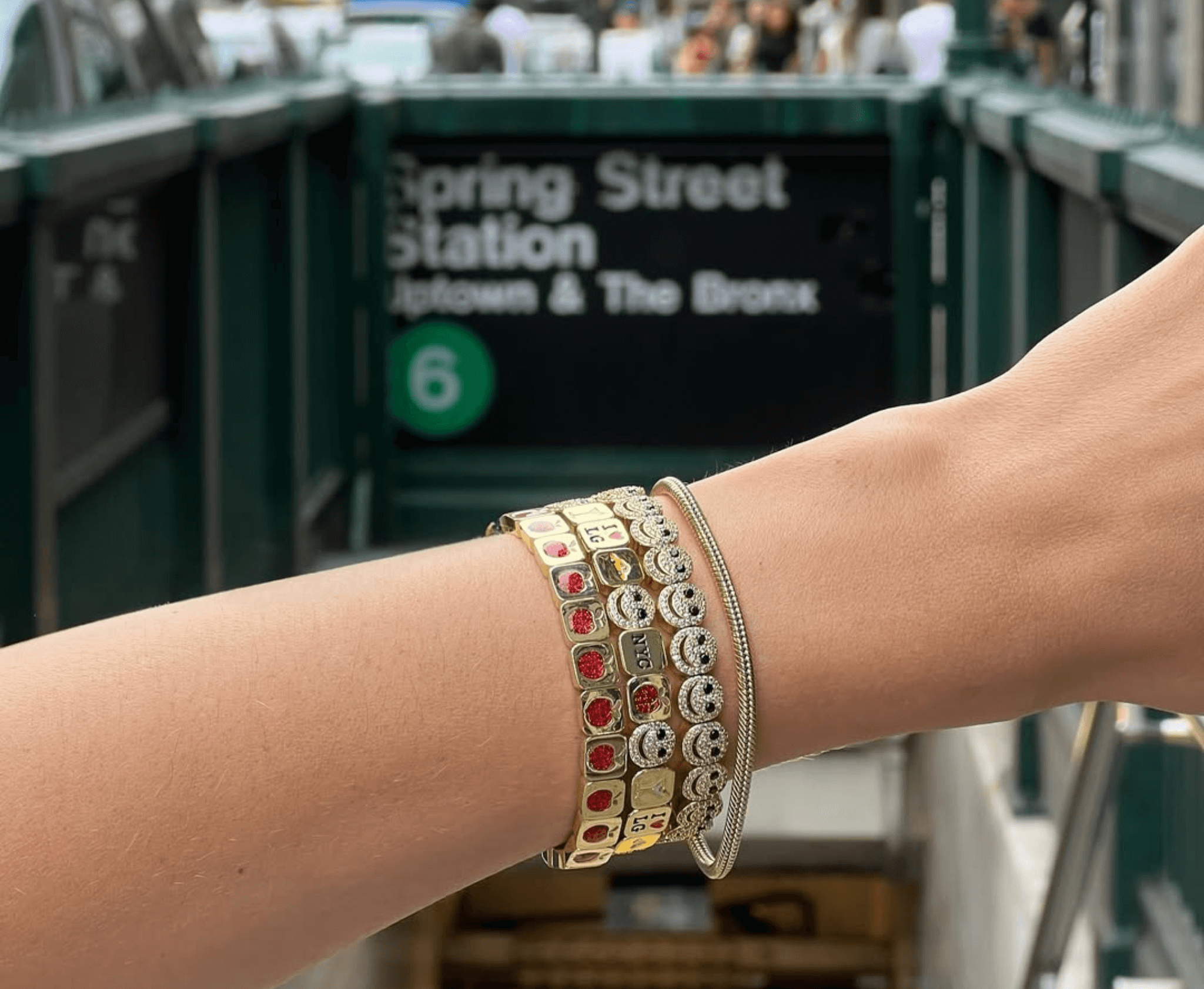 Close-up of a wrist with multiple charm bracelets in an urban setting